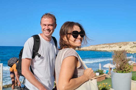 Middle-aged couple walking holding hands, man and woman traveling together. Summer vacation at sea