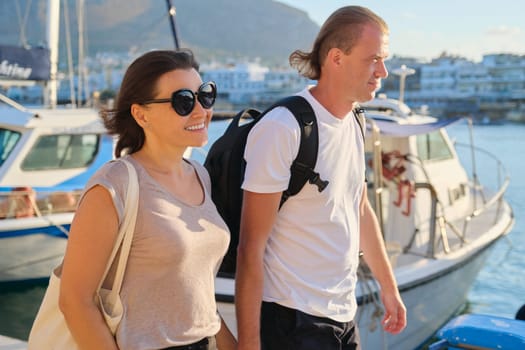 Middle-aged couple walking holding hands, man and woman traveling together. Summer vacation at sea