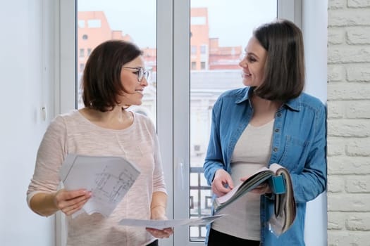 Female designer and client working with fabric samples. Selecting fabrics and design of curtains, females near window with sketch and materials