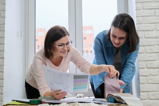 Female designer and client working with fabric samples. Selecting fabrics and design of curtains, females near window with sketch and materials