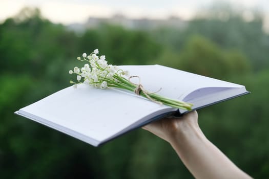 Small bouquet of lilies of the valley with craft rope in an open notebook in woman hand