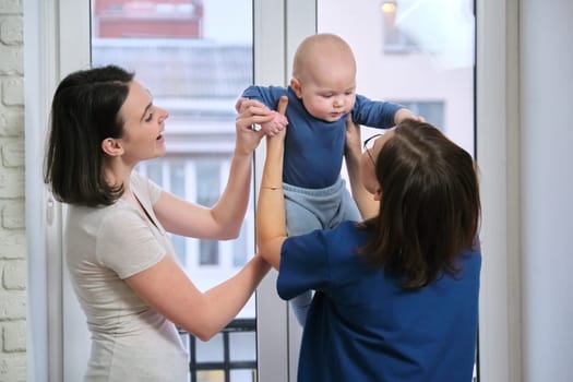 Visit of doctor pediatrician home, mother with baby son of seven months talking with doctor. Examination of child, health and childcare up to one year