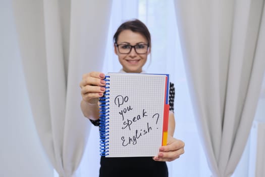 Smiling adult woman English teacher, female holding notepad in hand with text do you speak english. E-learning, private lessons, online training