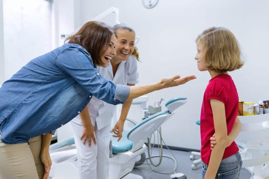 Happy mother and child daughter in office with dentist doctor after dental treatment. Beautiful smooth healthy white teeth in children