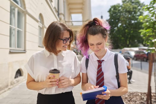 Walking and talking woman teacher with cup of coffee and student teenager, girl seeking advice from tutor