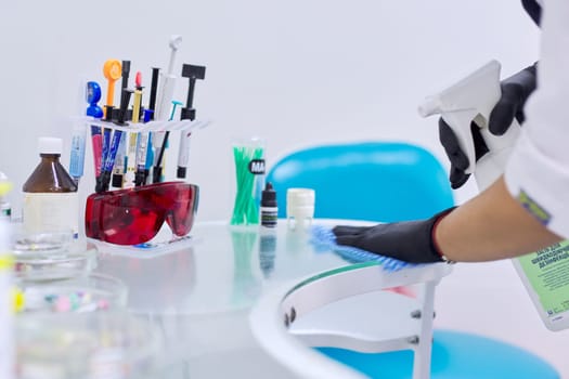 Kyiv UA, 31-07-2019. Hands of nurse sterilizing surface of dentist doctors work desk. Close-up of working desk in dentist office with dental composite sealing materials resins, various professional dental instruments tools and medicines