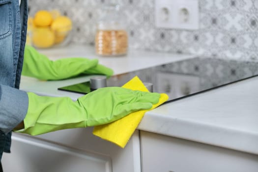 Close-up of cleaning kitchen, woman hands in gloves washing and cleaning electric hob in kitchen with rag