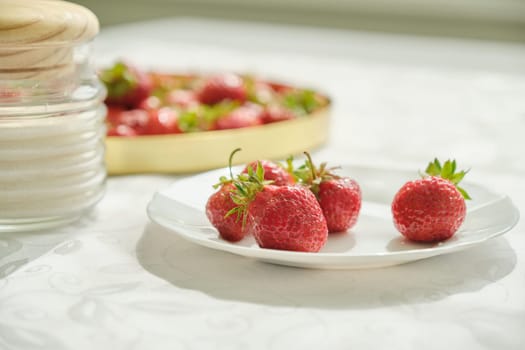 Delicious appetizing sweet strawberries, natural vitamins in the spring summer season. Berries on plate, jar of sugar on table at home