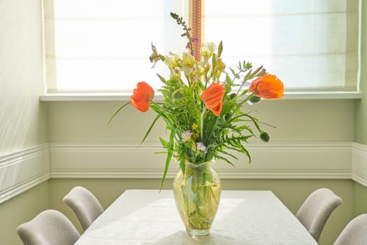Bouquet of spring summer flowers and red poppies in vase, standing on table in living room, dining area near window, copy space