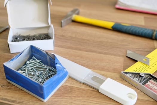 Hammer, nails, stationery knife with blade, screws for assembling furniture. Wood background, carpenter work tools