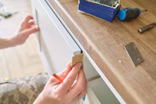 Closeup process of assembling kitchen furniture, hands of male worker. Working hands of male carpenter assembling furniture