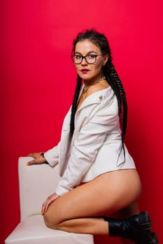 Beautiful female posing in a black underwear and white classic suit over red studio background.