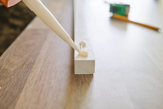 Carpenter male using construction glue when working with wooden white painted board, closeup, carpentry, woodwork, profession, people