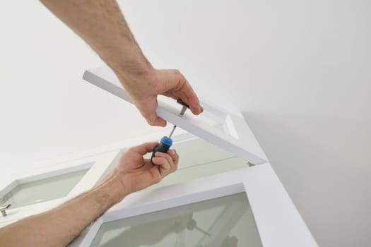 Working hands of male carpenter assembling furniture, close-up of installing door handles on door of kitchen cabinet