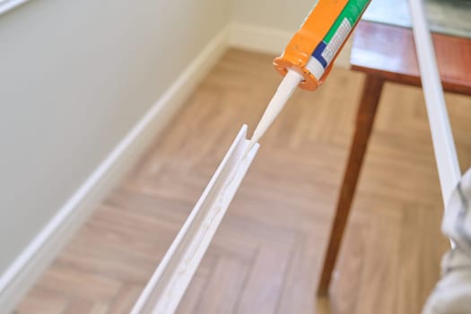 Carpenter male using construction glue when working with wooden white painted board, closeup, carpentry, woodwork, profession, people