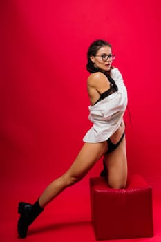 Beautiful female posing in a black underwear and white classic suit over red studio background.