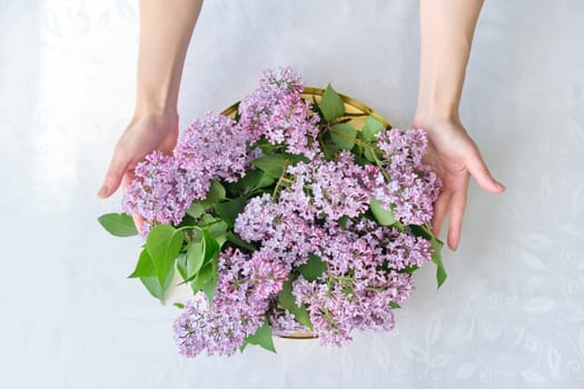 Floral decor of interiors, lilac flowers in form of bouquet on round golden tray. Spring seasonal flowers, woman hands holding bouquet, purple color