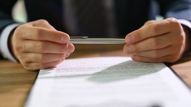 Businessman holding ballpoint pen in hands and studying information on document before signing at work in office closeup. Control of banking services concept