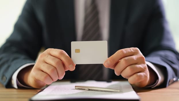 Businessman holding plastic credit bank card in hands at work in office closeup. Purchase and payment concept.