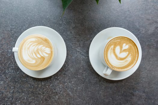 Two white cups of coffee art on gray stone countertop.