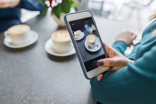 Coffee art, hands of woman taking photos on the phone two cups with latte art, background gray stone surface of the table coffee shop