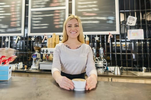 Freshly prepared cup of coffee art in hands of woman barista, girl standing near the coffee machine