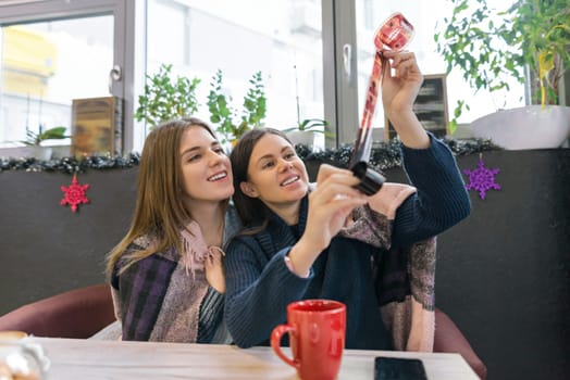 Winter lifestyle girls in cafe having fun looking at old film rolls, sitting at the table with hot drinks,girls under plaid on winter holiday