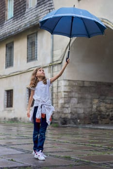 Little girl child in the rain with an umbrella, tourist old city background.