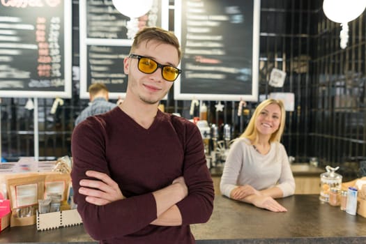 Young team of three cafe workers, people posing and smiling at coffee bar near bar counter. Teamwork, staff, small business, people concept.