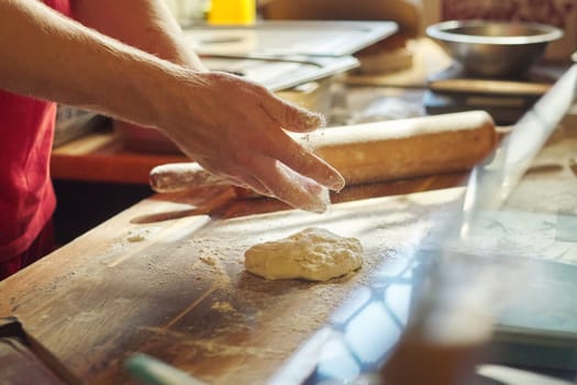 Hands of male baker with flour dough preparing food on wooden table. Cooking process, culinary, recipe, home bakery.