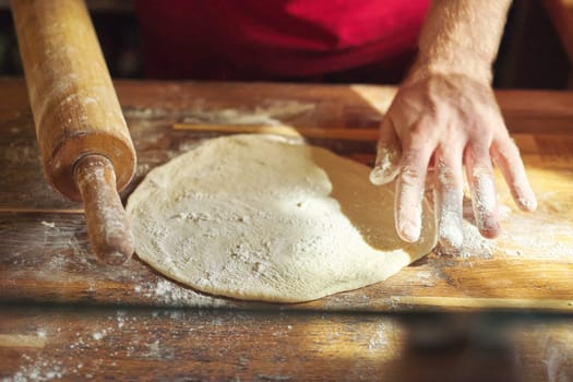 Hands of male baker with flour dough preparing food on wooden table. Cooking process, culinary, recipe, home bakery.