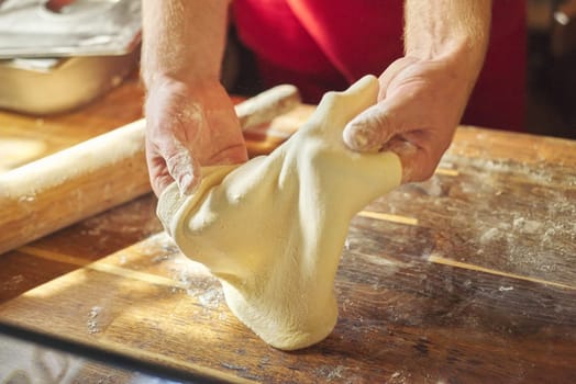 Hands of male baker with flour dough preparing food on wooden table. Cooking process, culinary, recipe