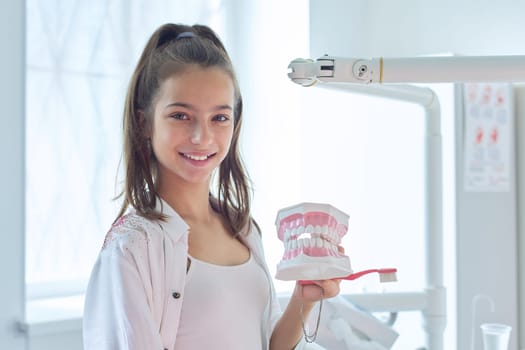 Smiling teenager girl in dental office holding jaw model with teeth in her hands