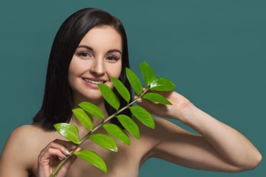 Closeup portrait of young beautiful woman with green leaf, female with natural beauty, no make-up, with extended eyelashes, green background