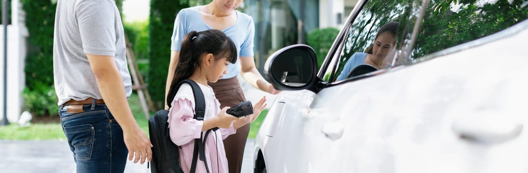 Progressive young happy family with electric vehicle and home backyard charging station. Green and clean energy from electric vehicles for healthy environment. Eco power from renewable source.