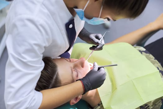 Female dentist treating teeth to patient, young man in chair at dental clinic