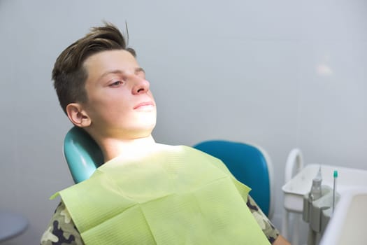 Boy sitting in dental chair at the clinic, teenager visits dentistry