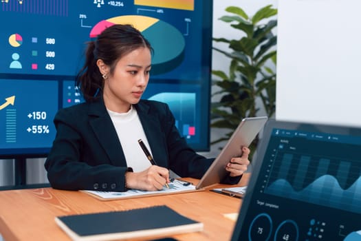 Focus portrait of female manger, businesswoman in the harmony meeting room with blurred of colleagues working together, analyzing financial paper report and dashboard data on screen in background.