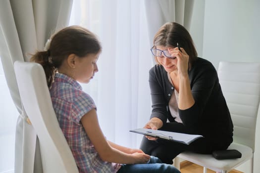 Talking girl and woman psychotherapist in office near window. Child psychology, mental health