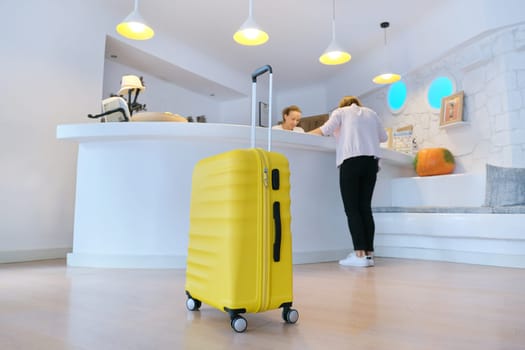 Concept of hotel business, travel, tourism. Yellow suitcase near reception desk in hotel lobby