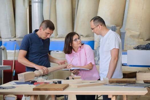 Group of industrial people client, designer or engineer and workers working together on project of wooden furniture. Teamwork in carpentry workshop.