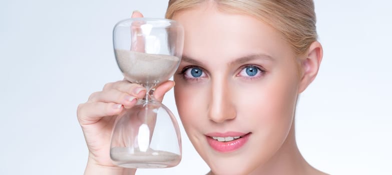 Closeup personable model holding hourglass in beauty concept of anti-aging skincare treatment. Young girl portrait with perfect smooth clean skin and flawless soft makeup in isolated background