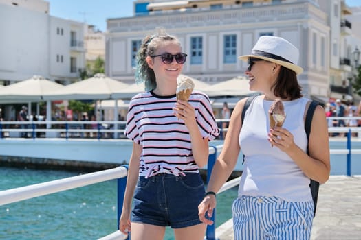 Melting ice cream in hands of smiling walking mother and daughter women on hot sunny summer day on seafront promenade