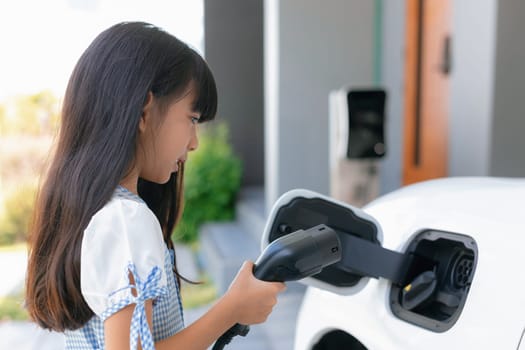 A playful girl holding an EV plug, a home charging station providing a sustainable power source for electric vehicles. Alternative energy for progressive lifestyle.