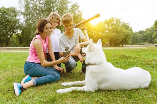 Children with dog on green grass rest in the park.