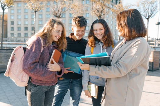 Mature female teacher talking to teenage students outside of school, golden hour.