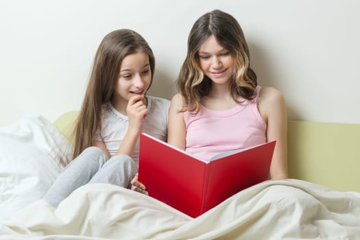 Two teenage girls sitting at home in bed look in school notebook. Communication and learning at home.