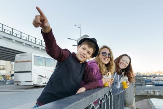 Lifestyle of adolescents, boy and two teen girls are walking in the city. Laughing, talking children eating street food, having fun. Background of the river embankment