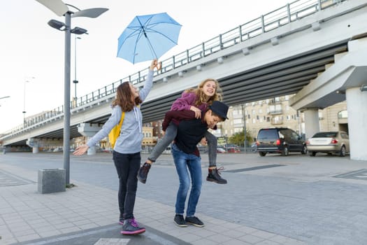 Group of teenagers friends having fun in the city, laughing kids with umbrella. Urban teen lifestyle