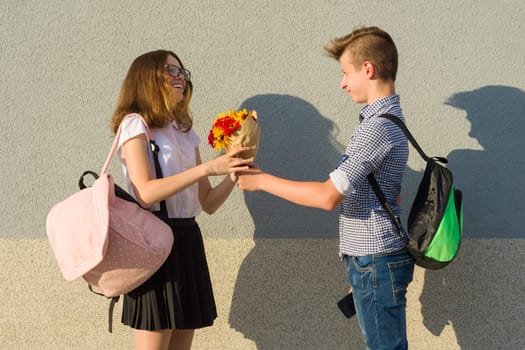 Boy gives girl bouquet of flowers. Outdoor portrait of couple teenagers.